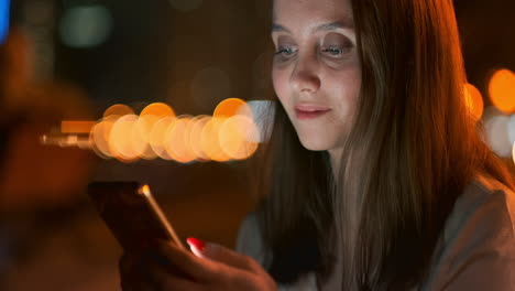 Una-Hermosa-Joven-En-Verano-En-Una-Gran-Ciudad-Nocturna-Mantiene-Un-Teléfono-Inteligente-En-Su-Interior-Y-Escribe-Un-Mensaje-Lee-Correos-Electrónicos-Y-Se-Comunica-En-Salas-De-Chat-Y-Redes-Sociales-Mantiene-Un-Blog-Mira-La-Pantalla-Del-Teléfono